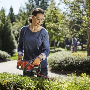 a woman trimming the top of a hedge