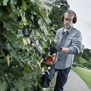 a man cutting the side of a hedge