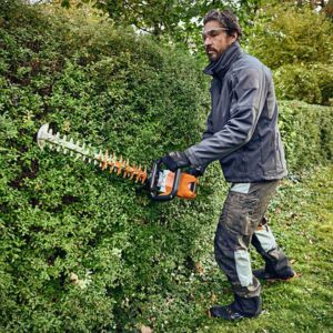 a man trimming the side of a hedge