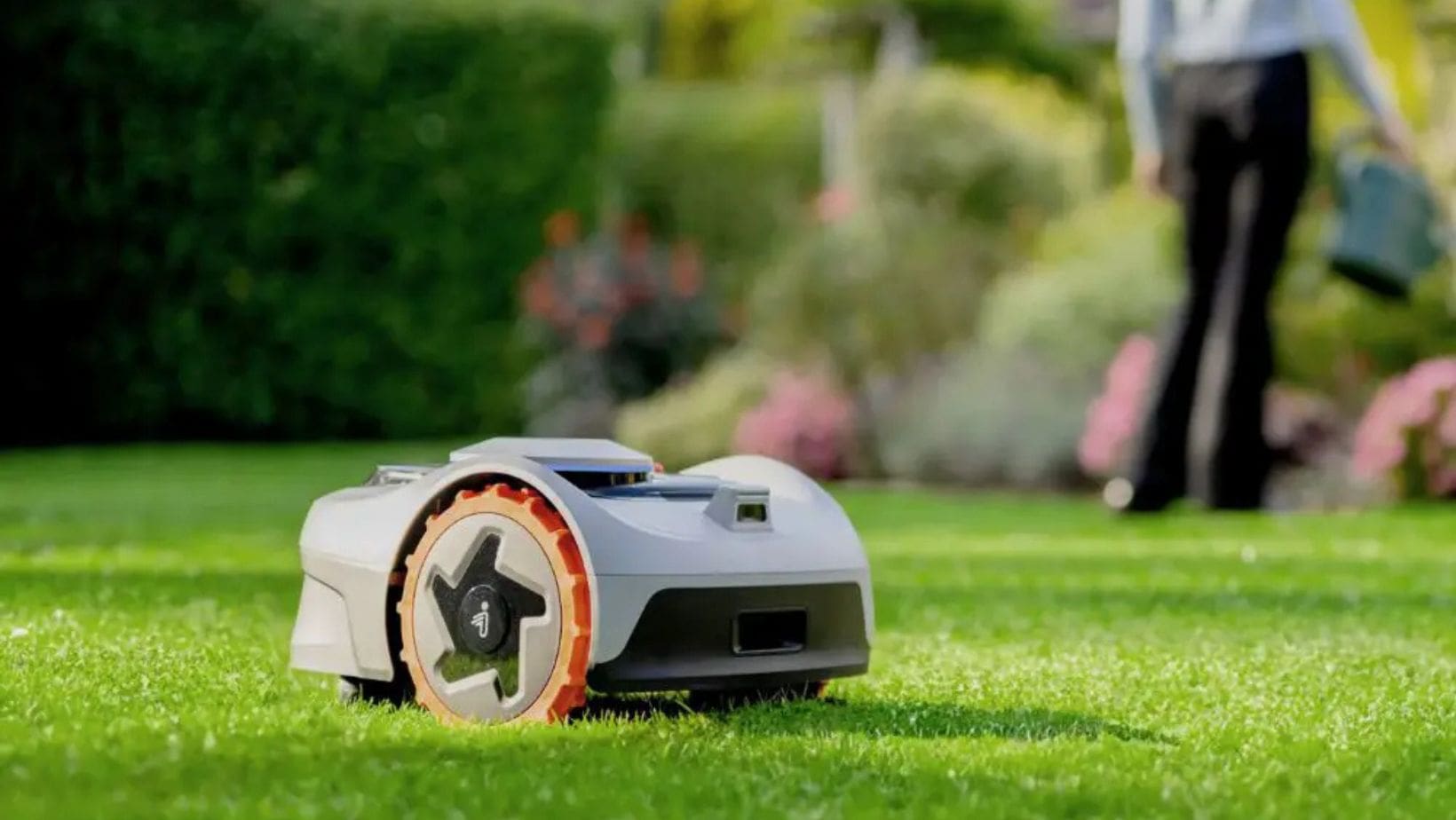 the Segway Navimow i105E Robotic Mower cutting grass with a woman in the background