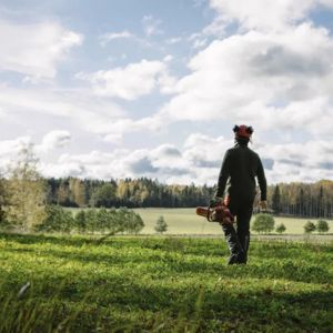 a man carrying a chainsaw, walking across a field