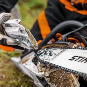 someone taking off a chainsaw's guide bar to tension the chain