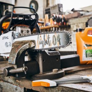 a chainsaw held in a vice, next to various tools