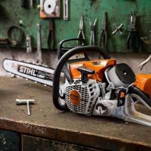 a chainsaw on a workbench, with various tools hanging on the wall behind it