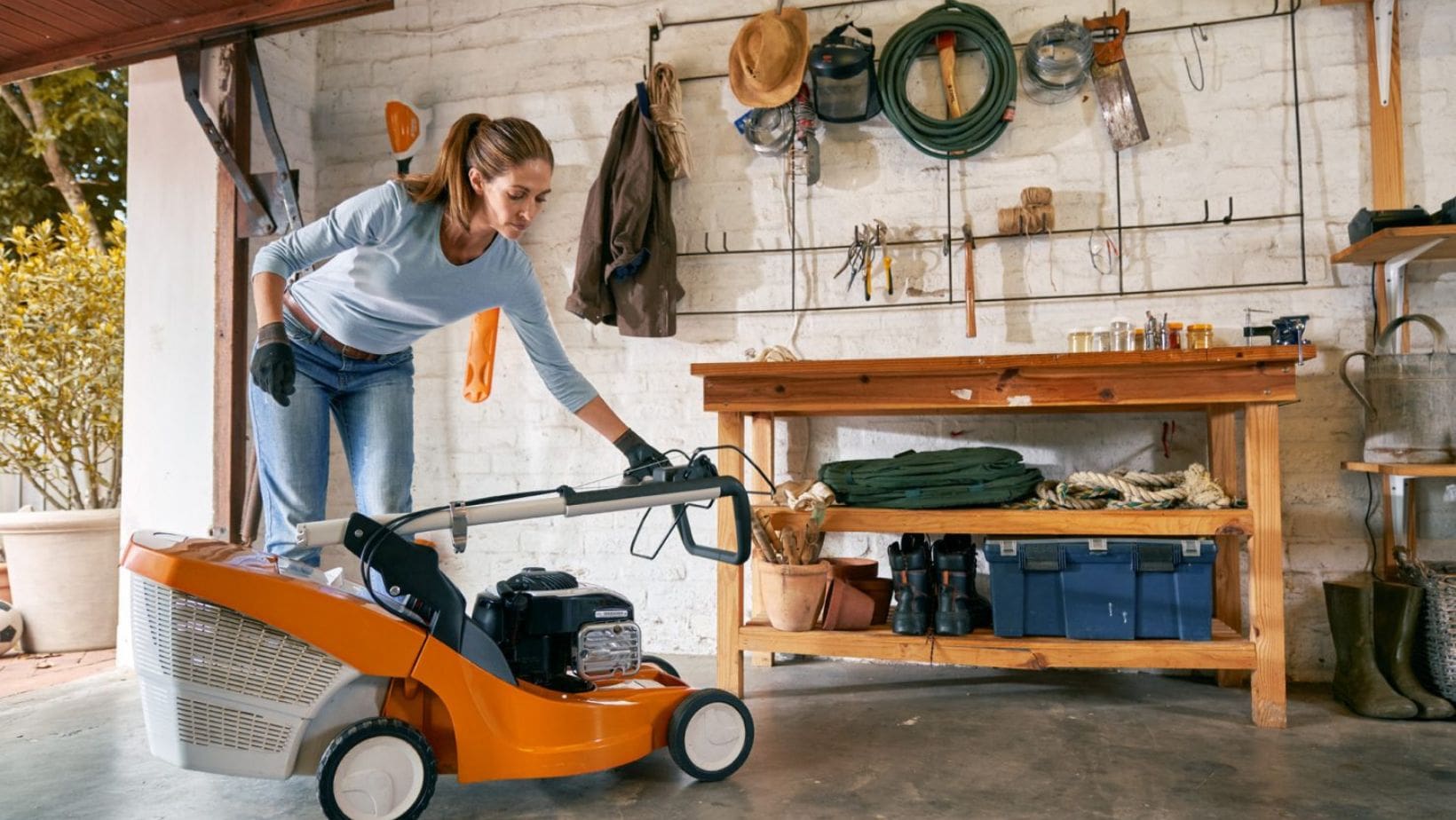 a woman storing a lawnmower in the shed for winter
