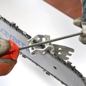 someone using a chainsaw file and file guide to sharpen a chainsaw