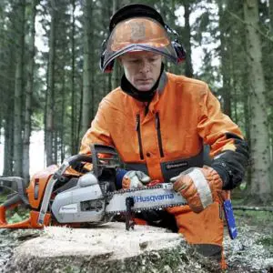 a man in orange overalls and a helmet sharpening a chainsaw in a forest