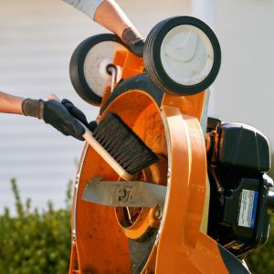 a woman cleaning the underside of an orange lawnmower with a brush