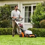a man mowing a lawn with an orange and white STIHL lawnmower