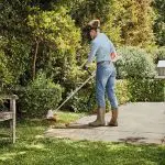 a woman using a strimmer to cut grass on the edge of a lawn