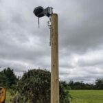 a robotic mower GPS reference station, on top of a wooden post, at the edge of a garden
