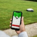 a man using a mobile phone app to control a robotic mower