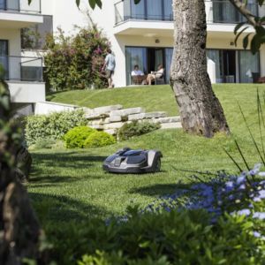 a Husqvarna robotic lawn mower on a lawn, in front of a house