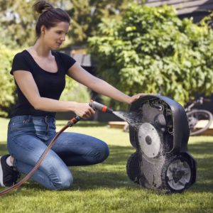 a woman hosing down the underside of a Husqvarna Automower