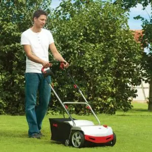 a man scarifying a lawn, using a white and red scarifier
