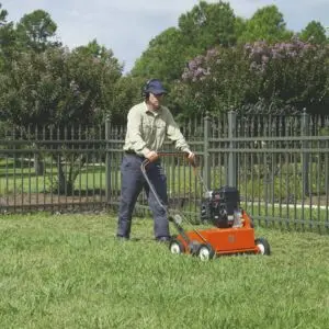 a man scarifying a patch of grass, which is enclosed by metal railings