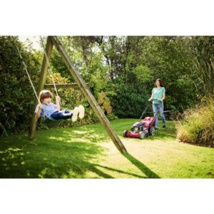 a woman mowing the lawn, near a child on a swing