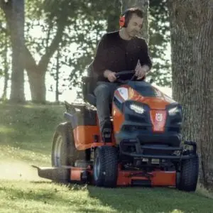 a man on a riding mower, close to some trees
