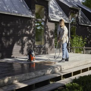 a woman pressure washing wooden decking outside a house