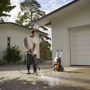 a man using the Husqvarna PW 240 Power Washer to clean a driveway