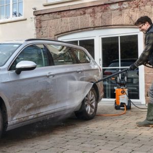 a man pressure washing a grey estate car outside a house