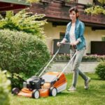 a woman mowing the lawn, using a STIHL orange mower