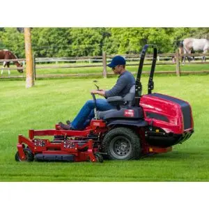 a man mowing a lawn using a red Toro zero turn, with horses in a paddock in the background