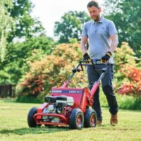 a man dressed in blue polo shirt and jeans, aerating a lawn in spring, using a Camon LA25 Petrol Lawn Aerator