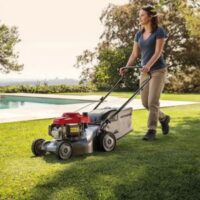 a woman mowing a lawn in spring, near to an outdoor swimming pool, using the Honda Izy HRG 416 PK Petrol Lawnmower