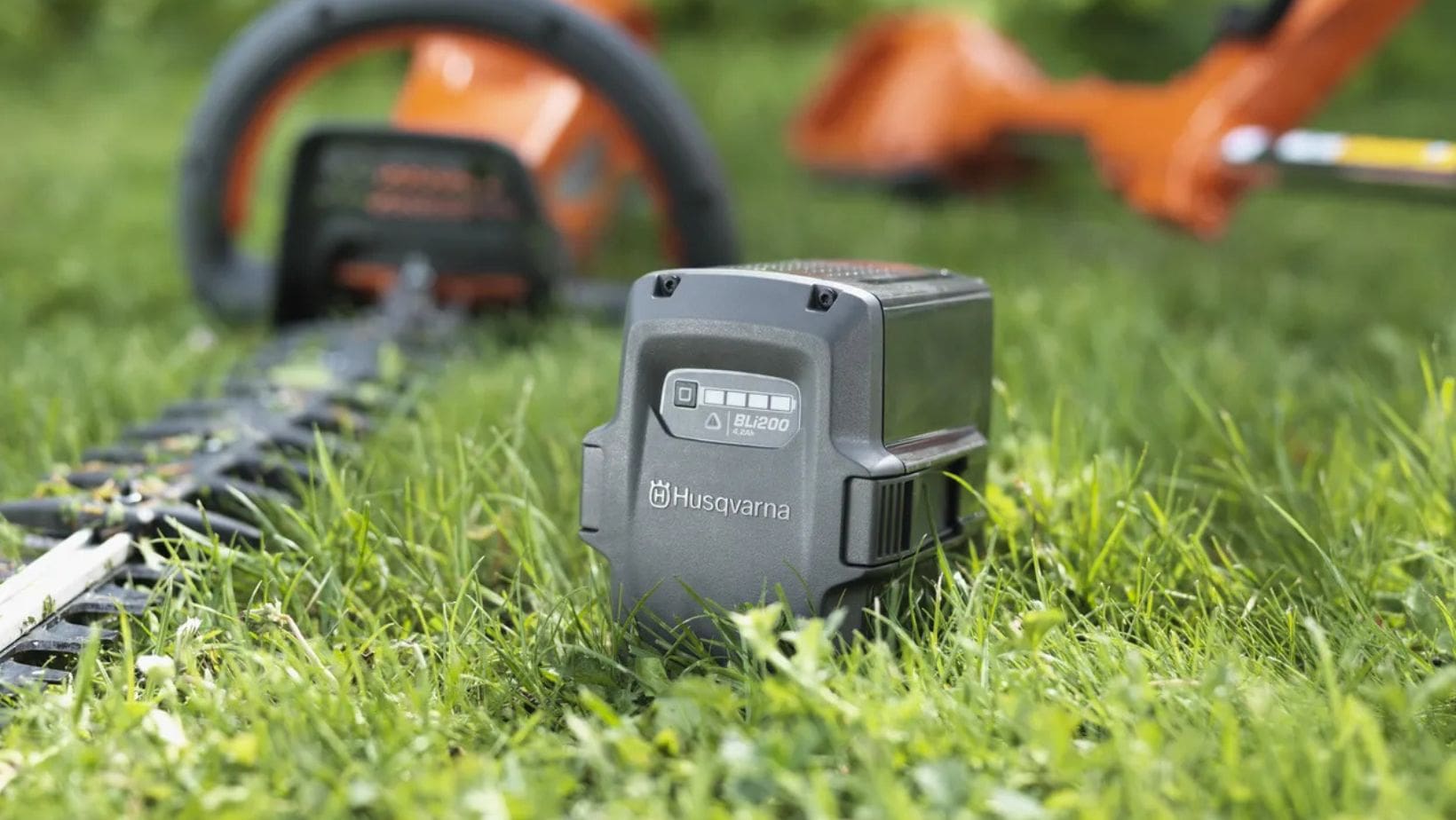 Husqvarna cordless tool-min a Husqvarna battery and 2 cordless garden tools laid on grass
