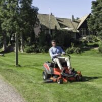 a man mowing the lawn in spring, using a Husqvarna ride-on mower, with a tree and house in the background