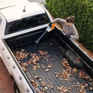 a woman using the STIHL BGA 30 Cordless Blower to tidy up leaves in the back of a white pick-up truck