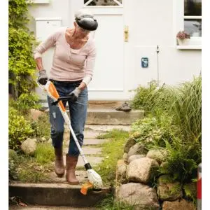 a woman using the STIHL FSA 45 Cordless Grass Trimmer to cut grass at the side of a step, outside a house