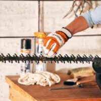 someone wearing STIHL-branded gloves, cleaning a hedge trimmer blade