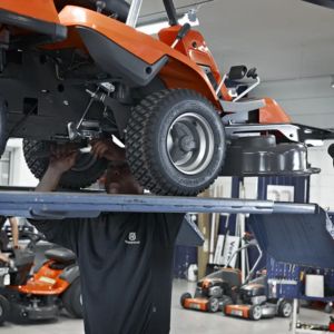 a Husqvarna mechanic stood working on the underside of a Husqvarna ride-on mower