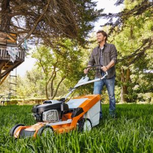 a man operating a STIHL lawnmower near a tree, with other trees in the background