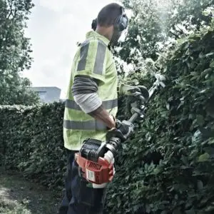 a man in a high-visibility jacket using a Husqvarna hedge cutter to trim a hedge
