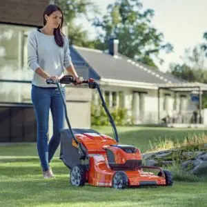 a woman with long, dark hair, mowing the lawn using an orange Husqvarna mower, with houses in the background