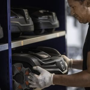 a man wearing white gloves, removing a Husqvarna Automower from a shelf