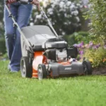 someone using a Husqvarna petrol mower next to a flowerbed