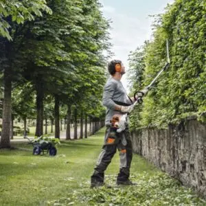 a man using the STIHL HL 94 C-E Petrol Long-Reach Hedge Trimmer to cut the side of a tall hedge