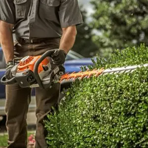 a man using the STIHL HS 82 Petrol Hedge Trimmer to trim a hedge