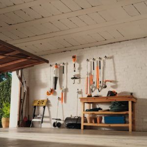 a selection of garden tools and machinery hanging on hooks on a white garage wall