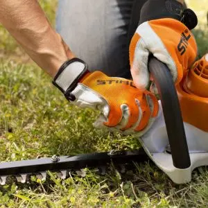 a man using a cloth to clean a STIHL hedge trimmer on a lawn 