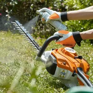 someone spraying a lubricant onto the blade of a STIHL hedge trimmer