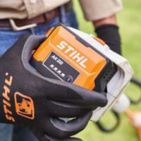 a man wearing a STIHL-branded glove, holding a STIHL AK 20 battery