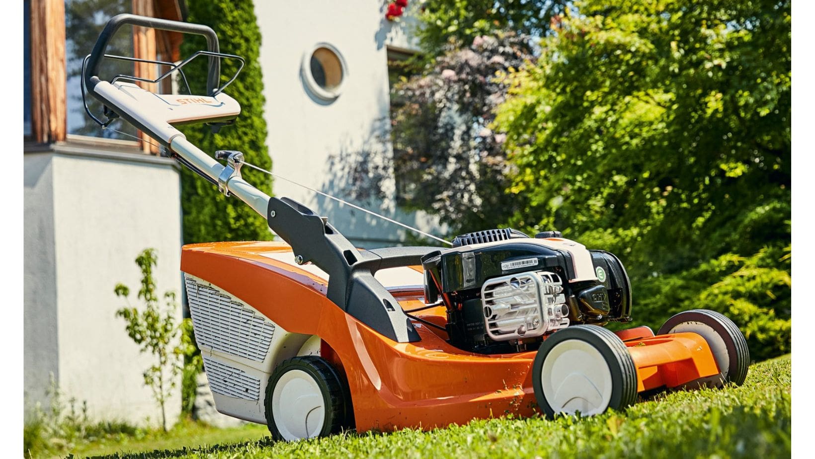 an orange STIHL petrol mower on a lawn, outside a house