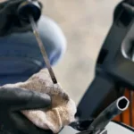 someone using a dipstick to check the oil level of a petrol mower