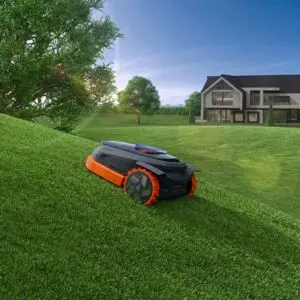 a Segway Navimow X315E Robotic Mower climbing a steep lawn, with a large house and trees in the background
