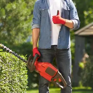 a man wearing red gloves, holding a hedge trimmer with one hand and putting his thumb up with the other